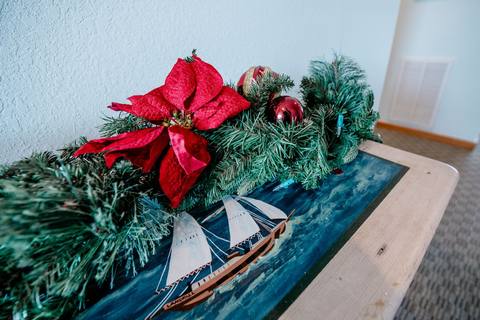 A poinsettia and pine garland with ornaments draped over a console table painted with a sailboat scene