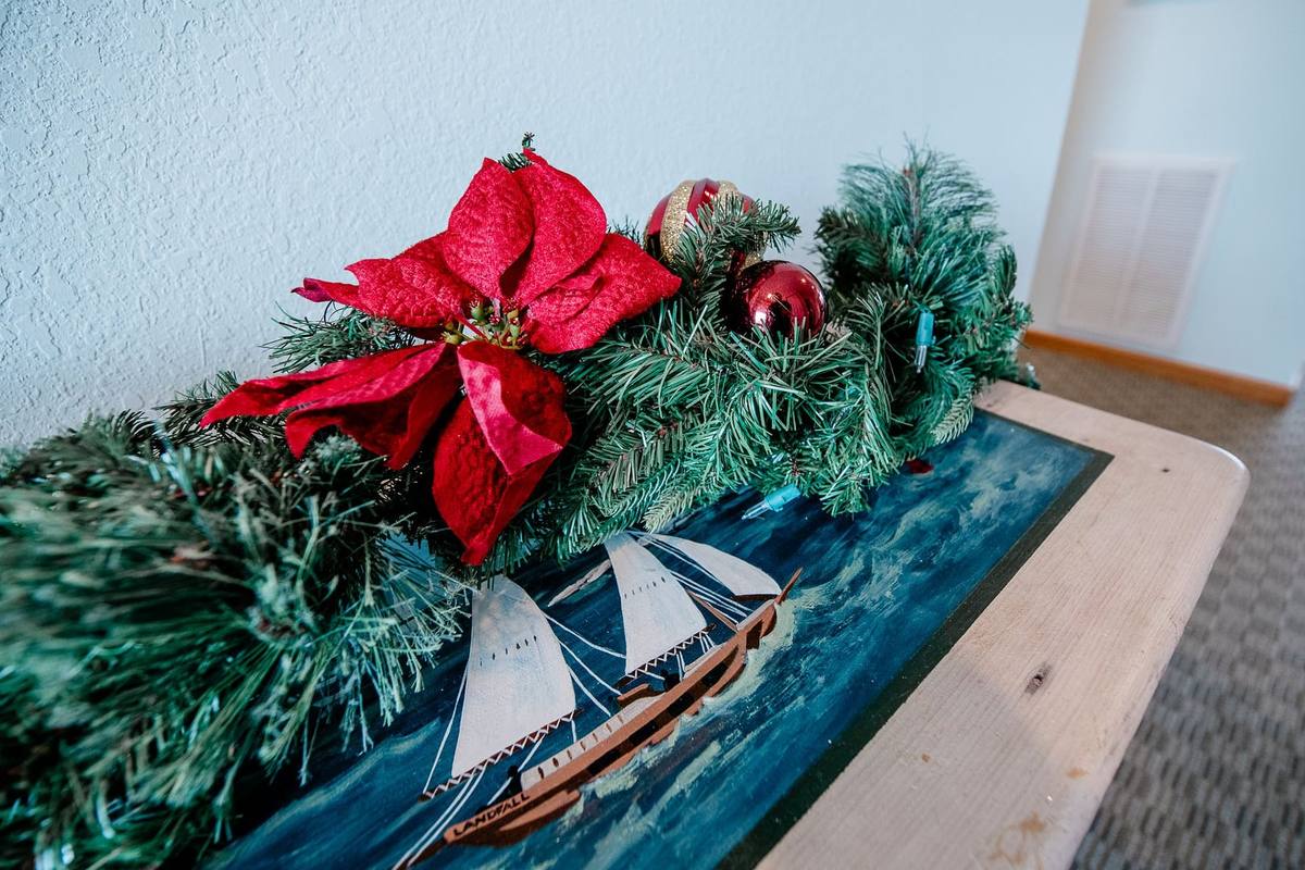 A poinsettia and pine garland with ornaments draped over a console table painted with a sailboat scene