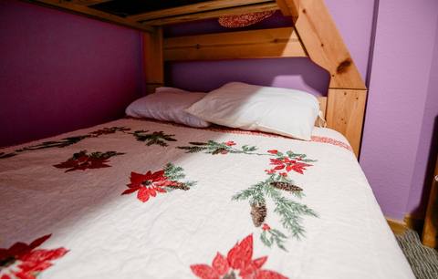Close-up of a white quilt with a red poinsettia and pinecone pattern on a wood bunk bed
