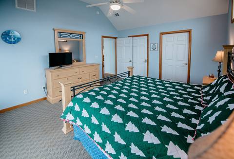 Light-blue primary bedroom with a vaulted ceiling and a king bed dressed in a dark green quilt patterned with white evergreen trees