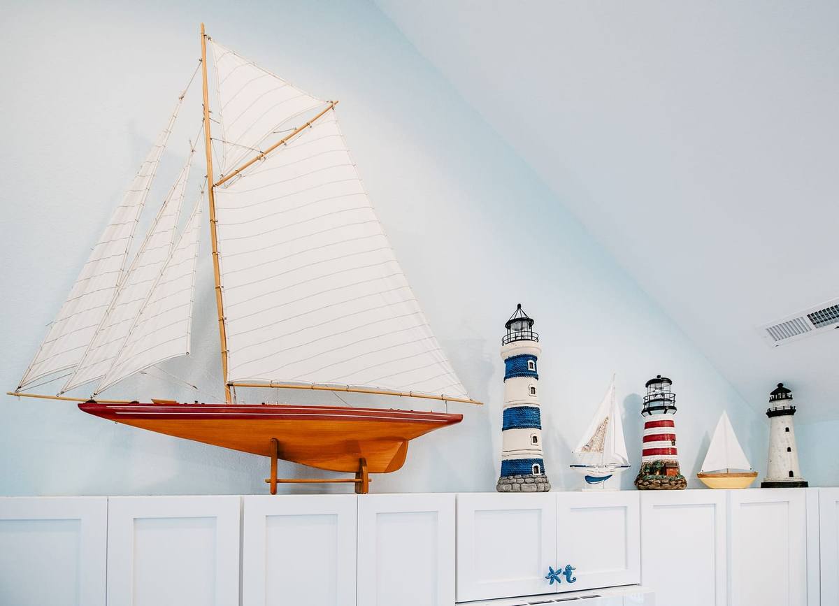 A large model sailboat and lighthouse figures on top of white cabinets