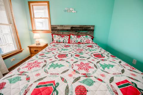 Seafoam-green bedroom with a bed dressed in a quilt patterned with red and green Christmas ornaments and mini trees