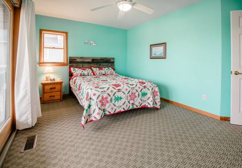 Seafoam-green bedroom with a queen bed dressed in a poinsettia and wreath print quilt, a reclaimed-wood headboard, and a window with white curtains