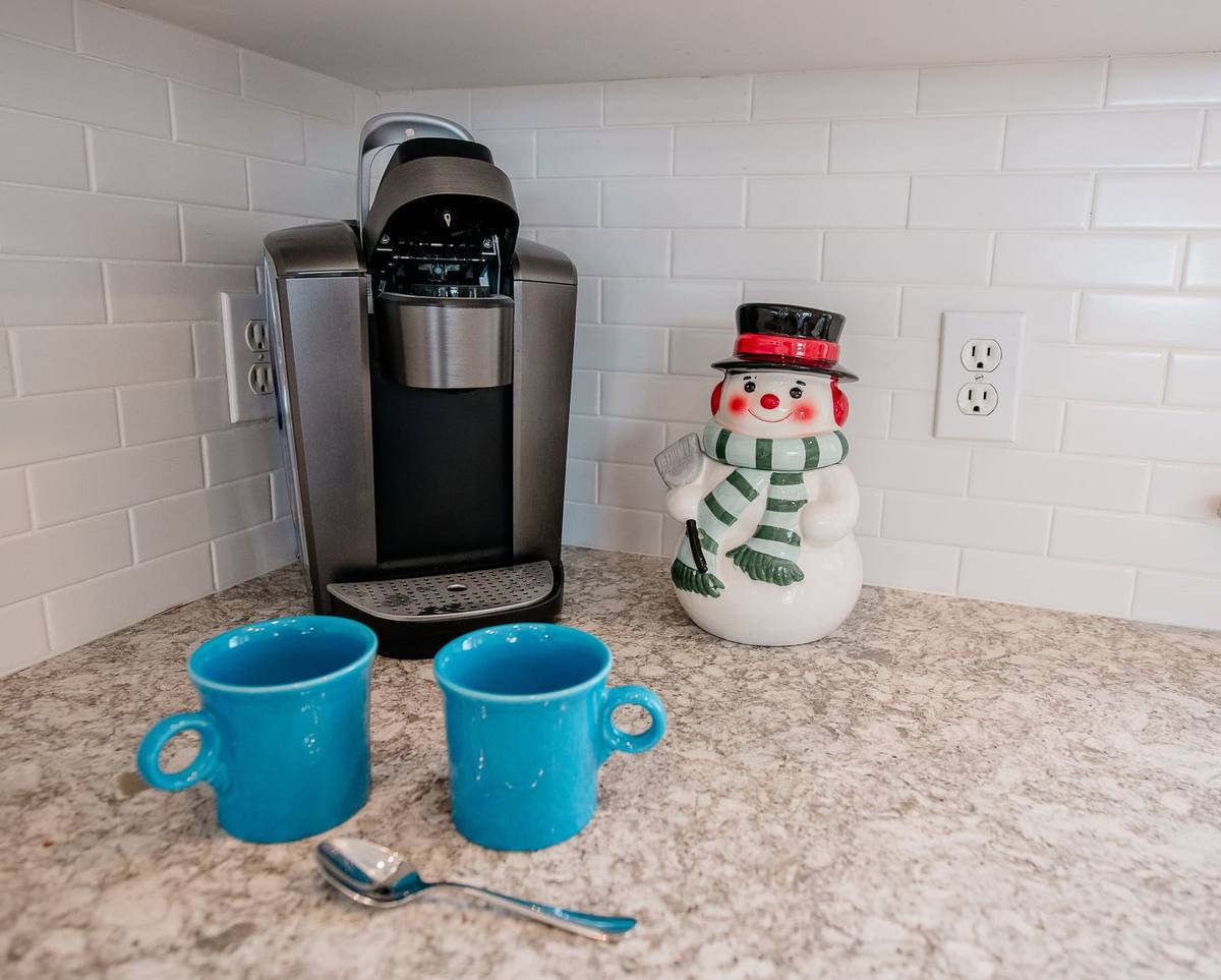 A smiling snowman cookie jar beside a Keurig coffee maker and two turquoise mugs on the kitchen counter