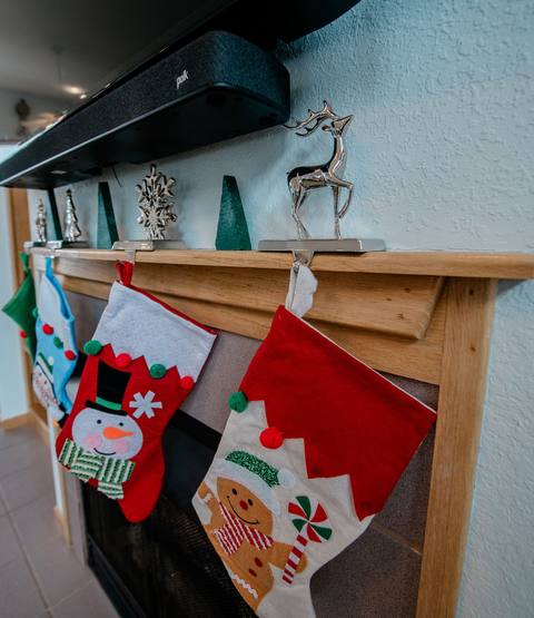Close-up of two Christmas stockings hanging from silver reindeer-shaped stocking holders on a wood mantle, with mini trees and a silver reindeer figurine above
