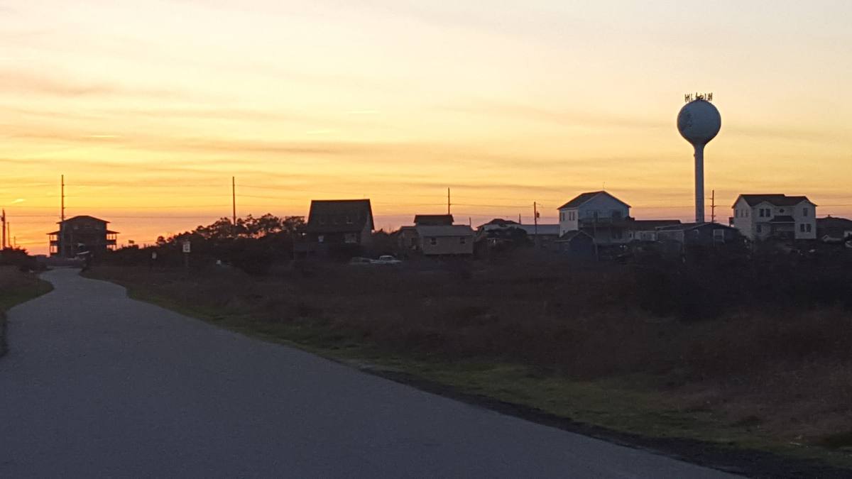 A colorful sunset sky over Corolla rooftops and a water tower