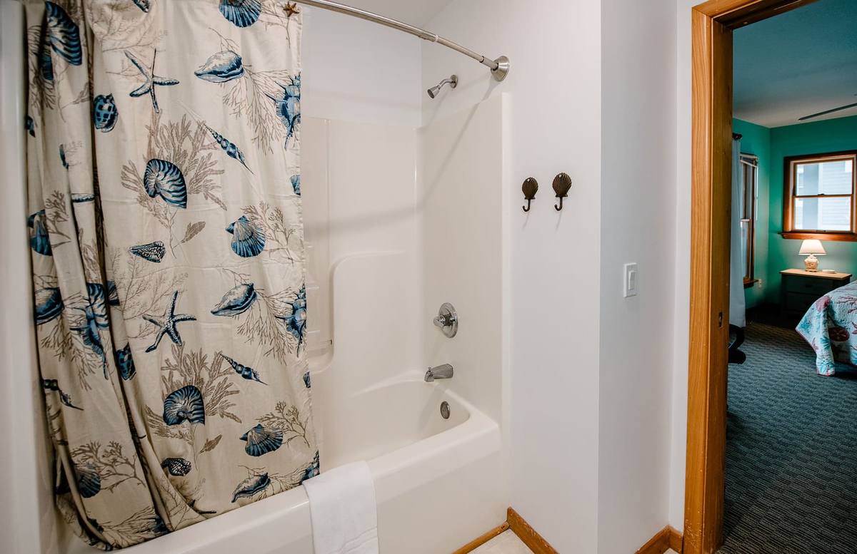 Shell-print shower curtain over a tub with the teal bedroom beyond