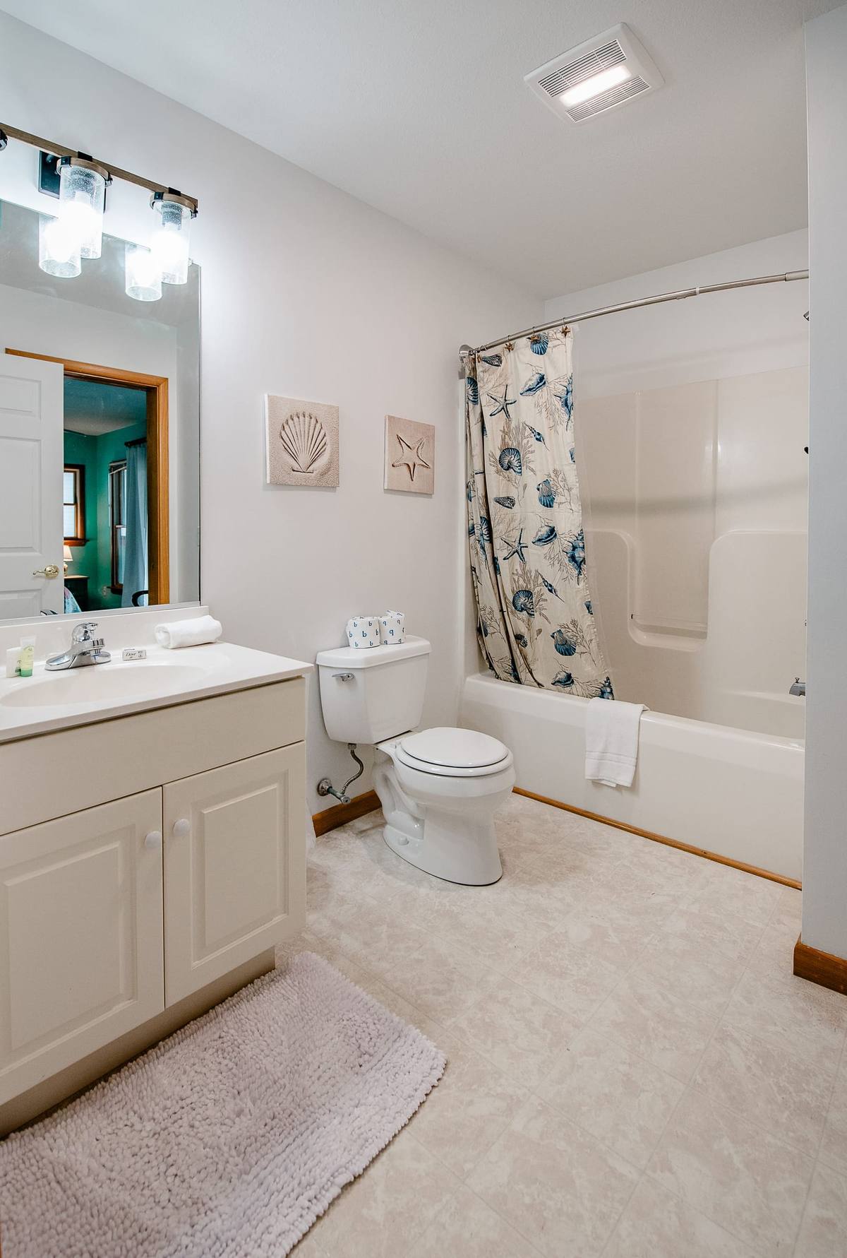 Bathroom with a tub-shower, shell curtain, and framed shell prints