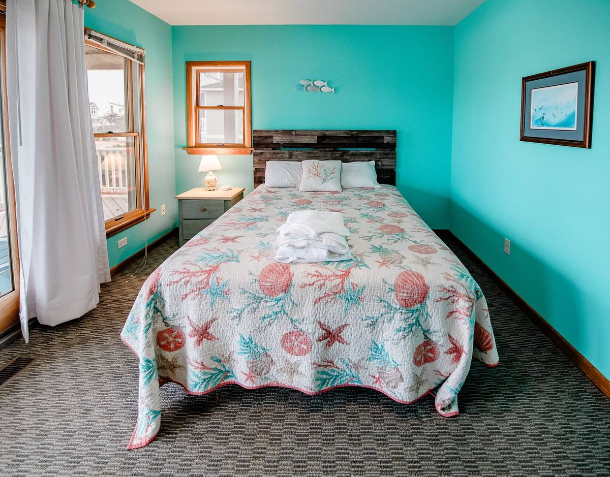 Teal bedroom with a bed in a coral and shell quilt and a driftwood headboard