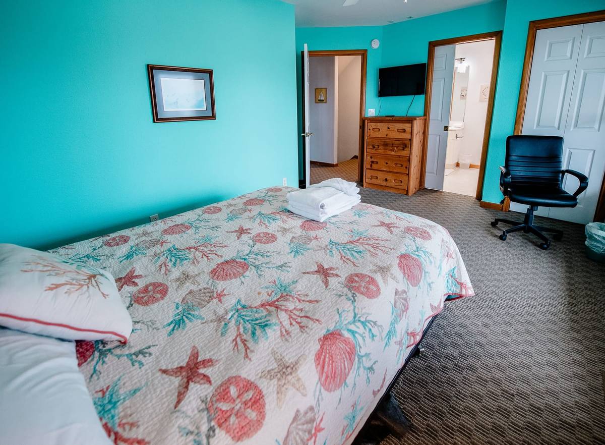 Teal bedroom with a dresser, TV, and an office chair by the bed