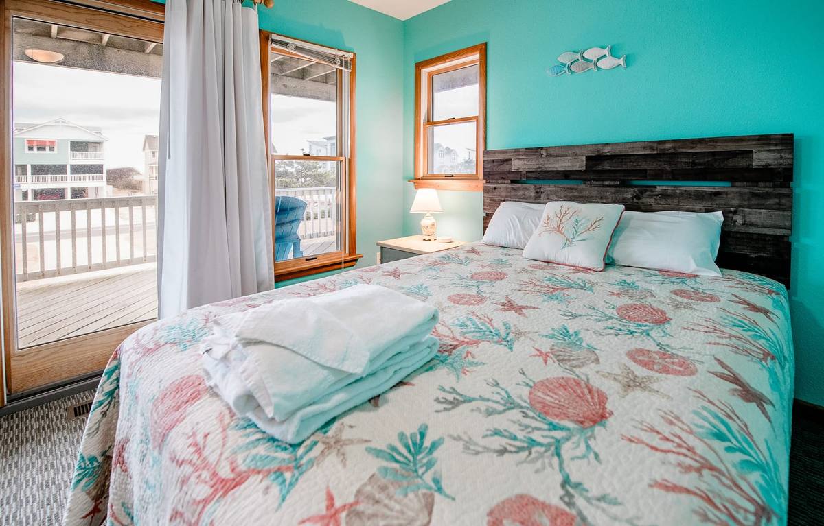 Driftwood headboard, coral pillows, and a deck view from the teal bedroom