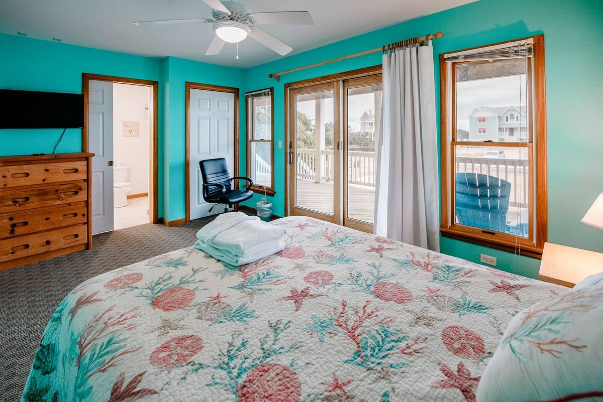 Teal bedroom with a dresser, TV, and sliding doors to the deck