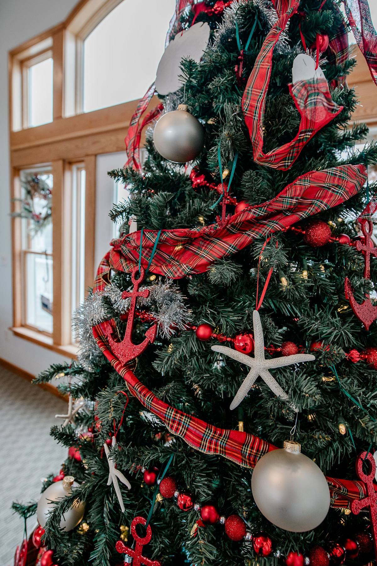 Close-up of Christmas tree branches decorated with a red starfish ornament, a red glitter anchor, silver ball ornaments, and red plaid ribbon