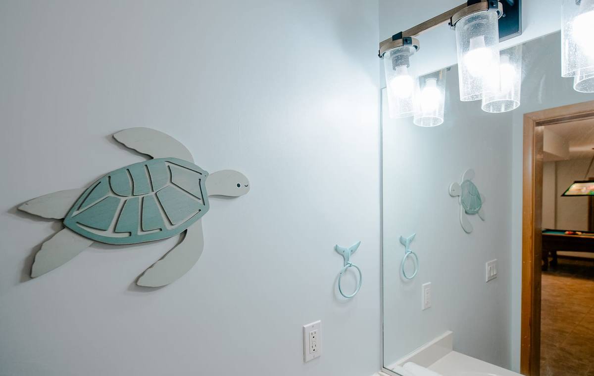 A large teal sea turtle on the bathroom wall with the game room beyond