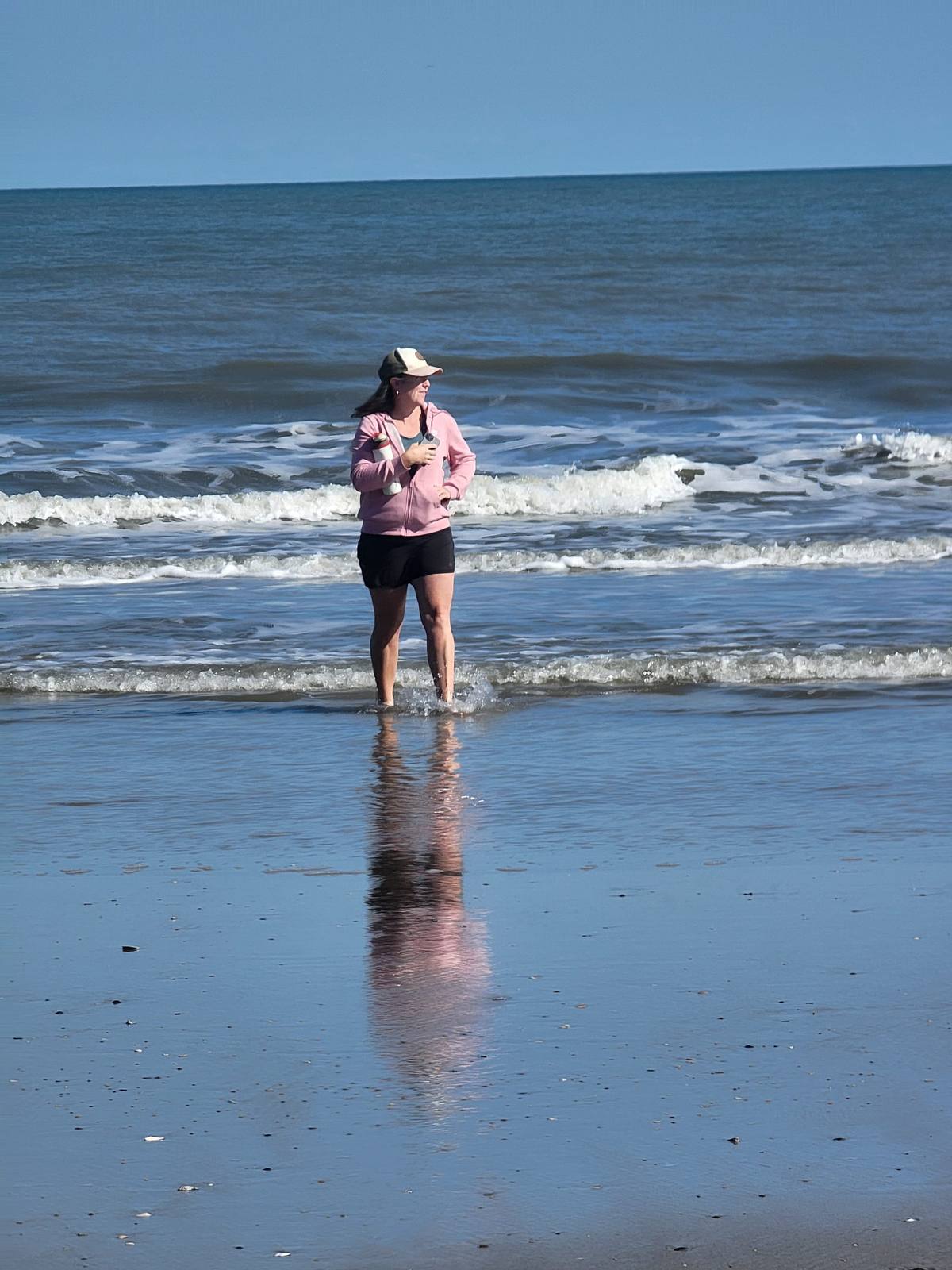 A woman wading and laughing in the surf on an empty beach