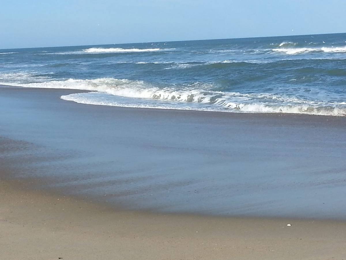 Small waves rolling up a wide, wet stretch of Outer Banks beach under a blue sky