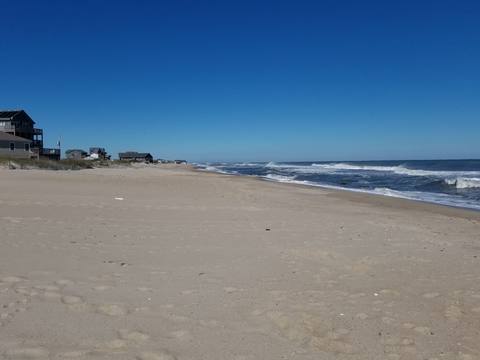 A wide, empty shoreline with gentle surf under a clear sky