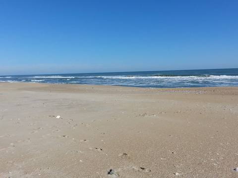 A wide, flat, empty beach meeting the ocean under a pale blue sky