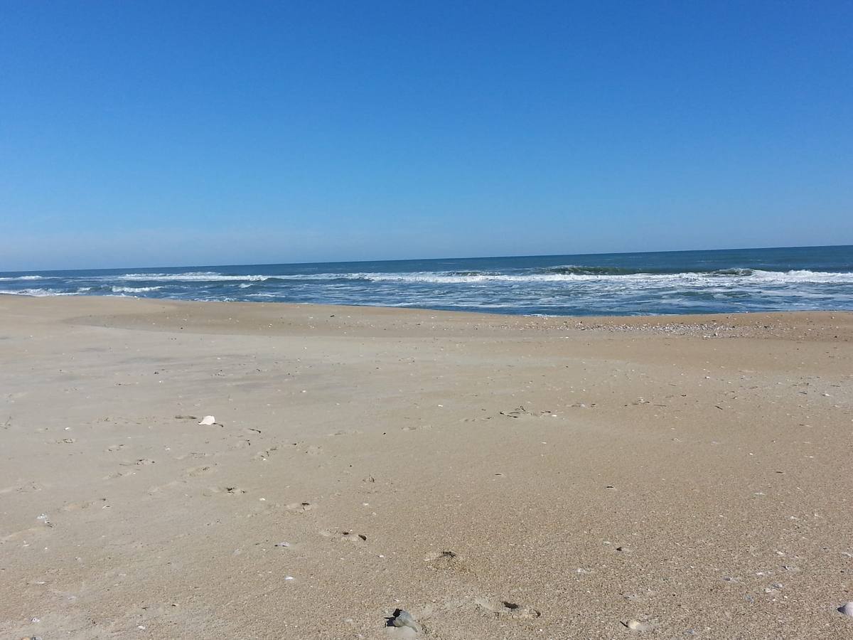 A wide, flat, empty beach meeting the ocean under a pale blue sky