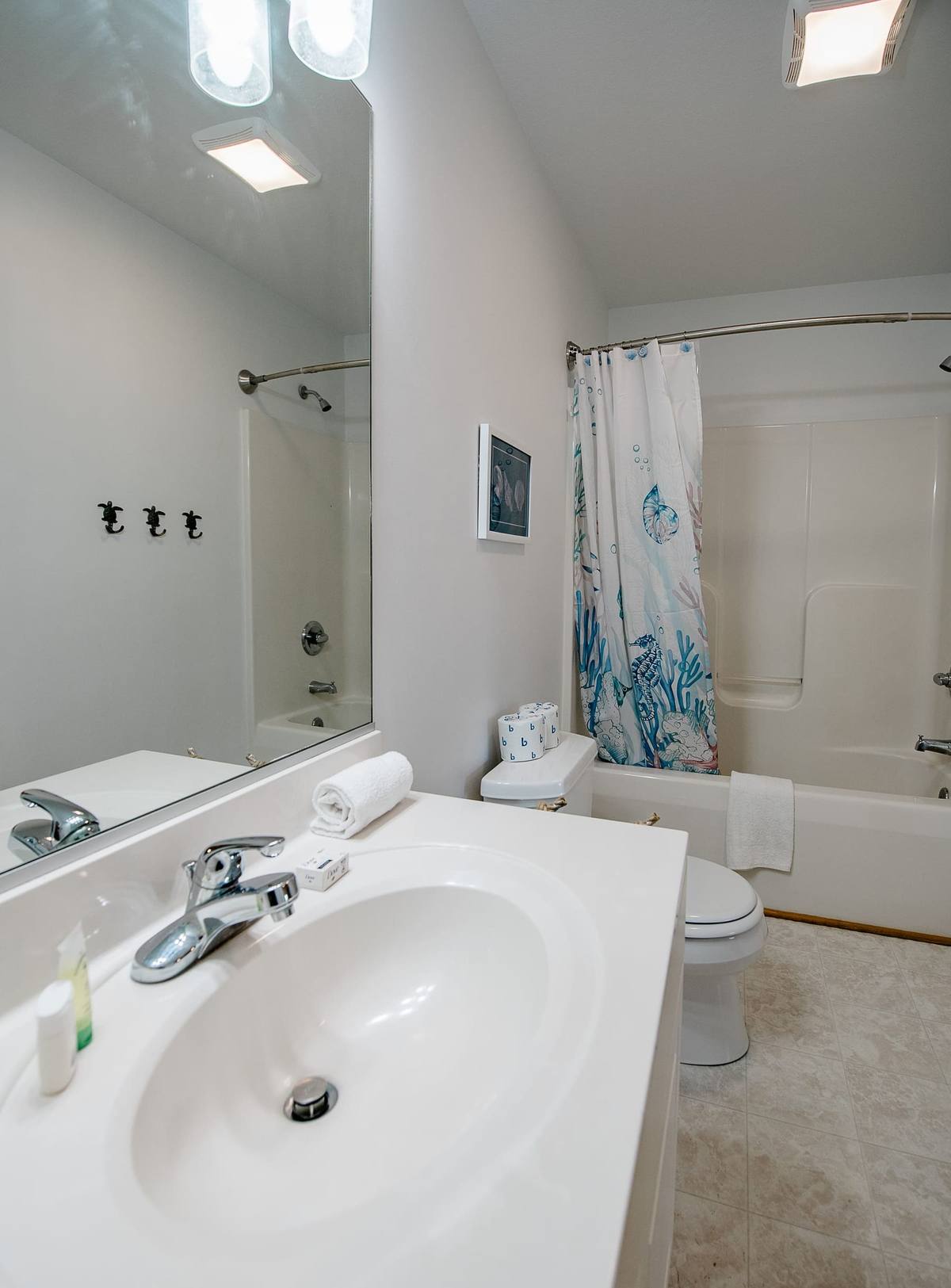 Bathroom with a tub, coral shower curtain, and three sea-turtle wall hooks