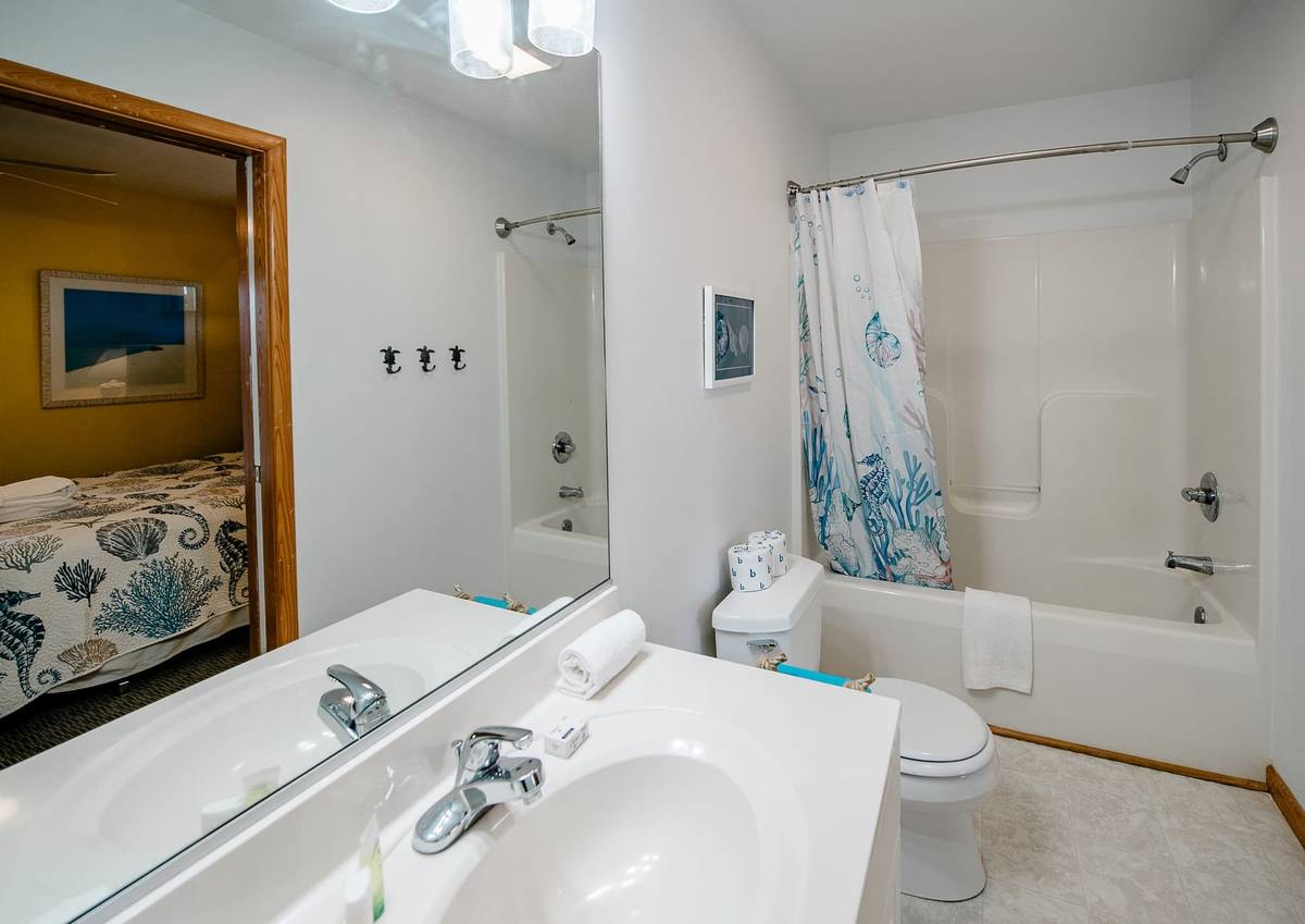 Bathroom with a tub-shower, coral-print curtain, and a view of the yellow bedroom