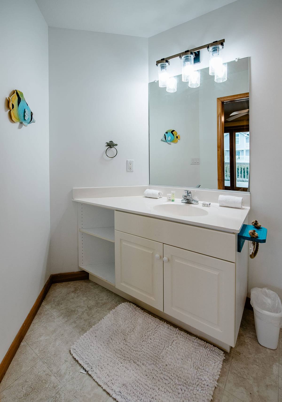 Bathroom vanity with open shelving and a colorful fish on the mirror