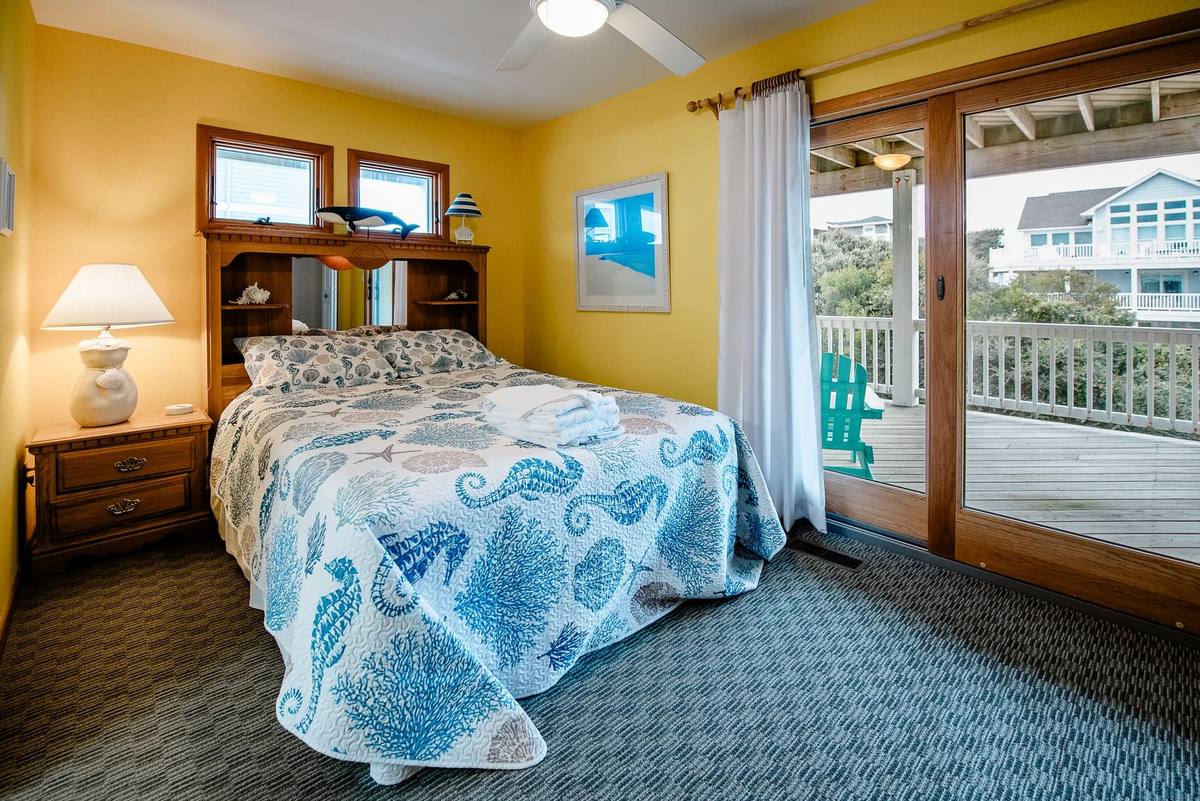 Yellow bedroom with sliding doors to a deck with a teal Adirondack chair