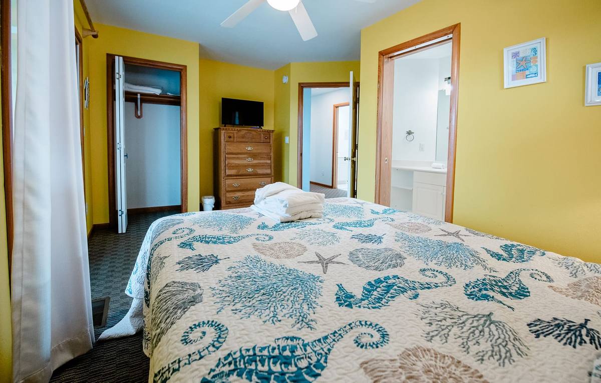 Yellow bedroom with a dresser and TV and a doorway to the bathroom