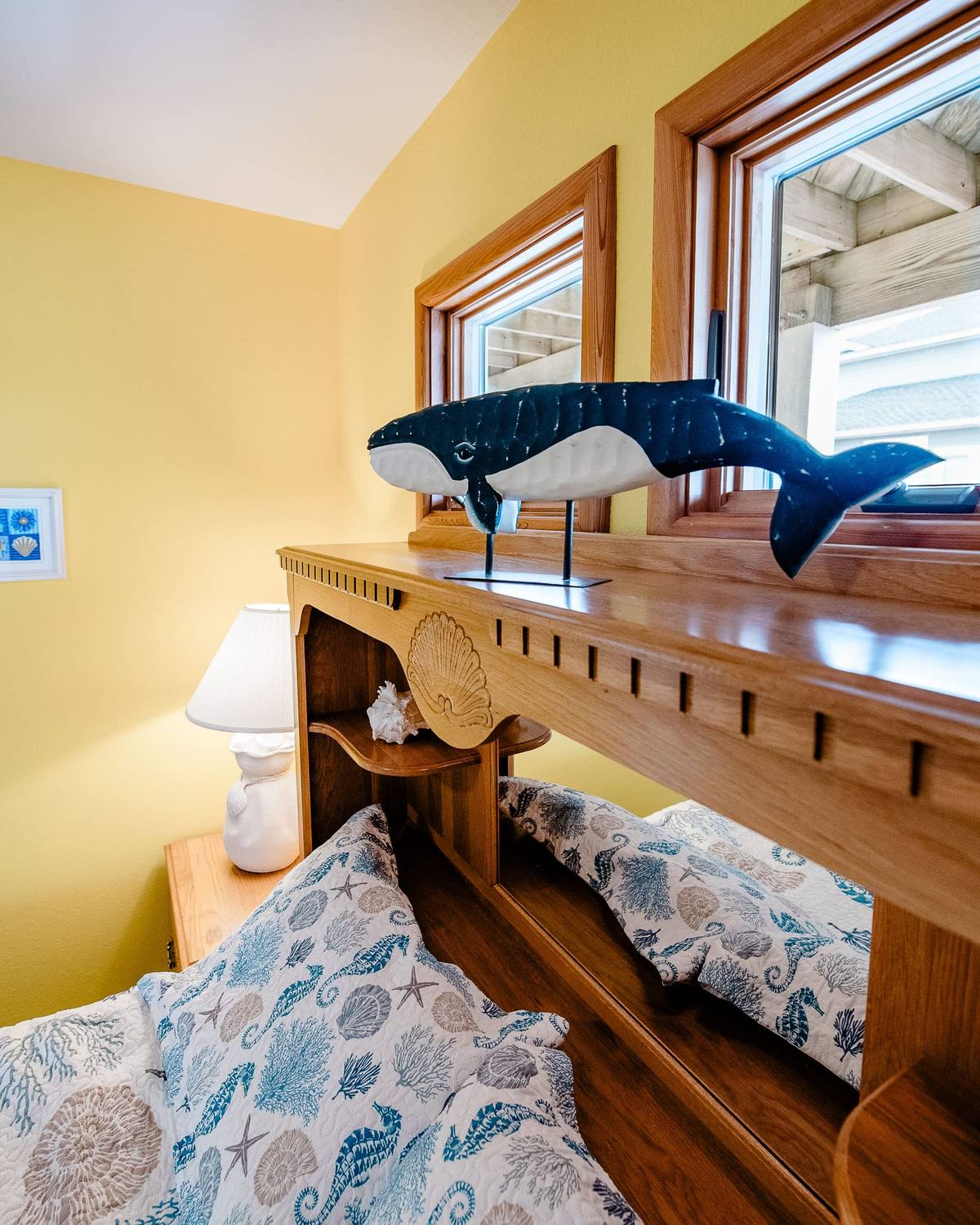 A carved whale figure on a wooden headboard with a shell lamp beside it
