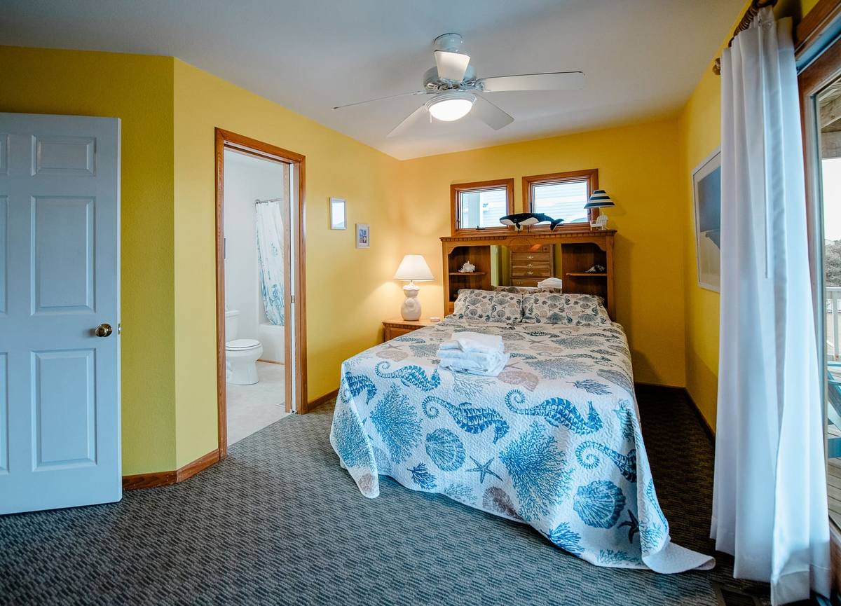 Yellow bedroom with a ceiling fan, seahorse-print bed, and a private bath